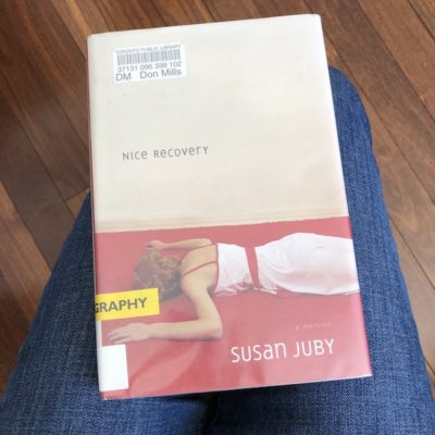 Susn Juby's memoir, Nice Recovery is shown. It features a woman wearing a white and red dress, lying face on a bed, with her arms out to either side.