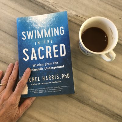 The book Swimming in the Sacred is shown beside a coffee cup.