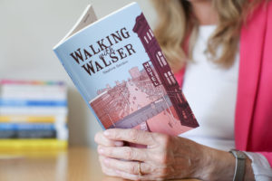 Daphne's hands are shown holding her paperback book. it's called Walking With Walser and features an illustration by Tom Chitty.
